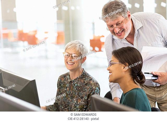 Smiling students talking at computer in adult education classroom