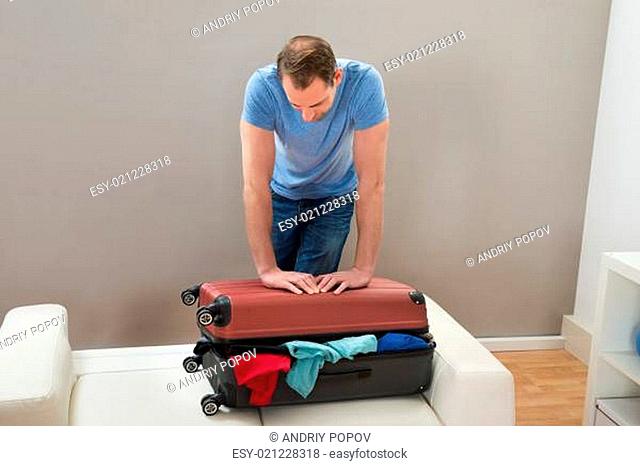 Mid Adult Man Trying To Close Suitcase With To Much Clothes