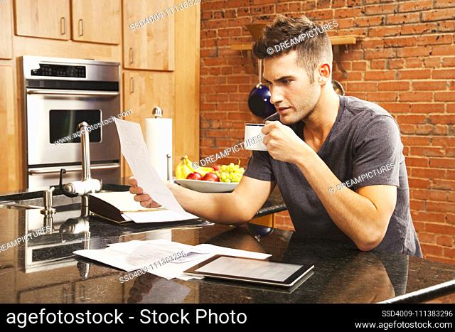 Caucasian man looking at paperwork in kitchen