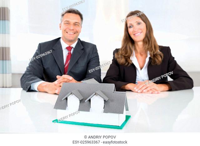 Two Happy Businesspeople Looking At House Model On Desk
