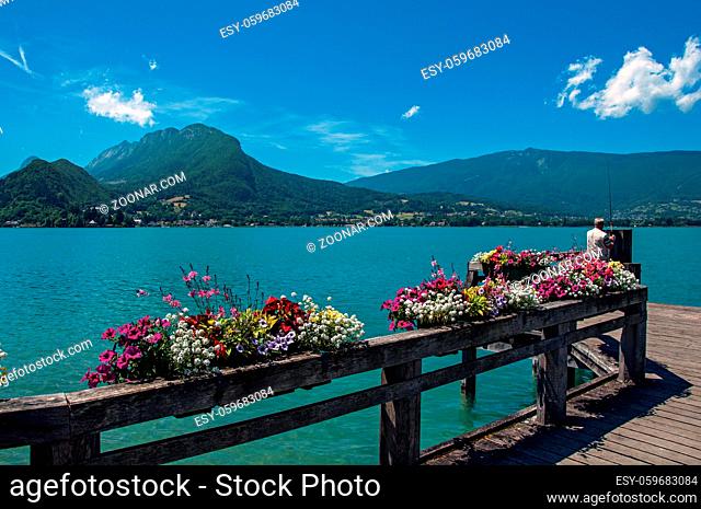 Pier with flowers on the Annecy Lake with blue sky mountains landscape. Near the lovely village of Talloires. Department of Haute-Savoie, southeastern France