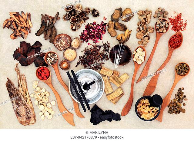 Chinese herbal medicine with traditional herbs, acupuncture needles, moxa sticks used in moxibustion therapy and mortar with pestle on hemp paper background