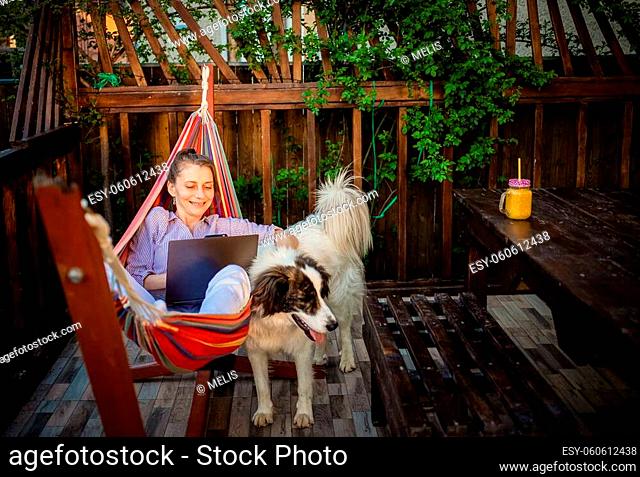 woman with laptop and white shepherd dog in backyard summer home office