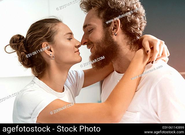 Romantic couple in love. Close up portrait. Young man kissing his wife standing at the kitchen. Morning kiss to a wife, young couple flirting in the kitchen