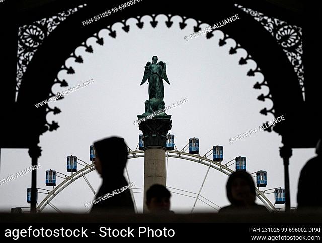25 October 2023, Baden-Württemberg, Stuttgart: Passers-by stand in the music pavilion on the Schlossplatz, in the background the jubilee column with the...
