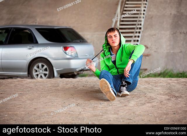 Sad young man in depression sitting on the ground next to his car
