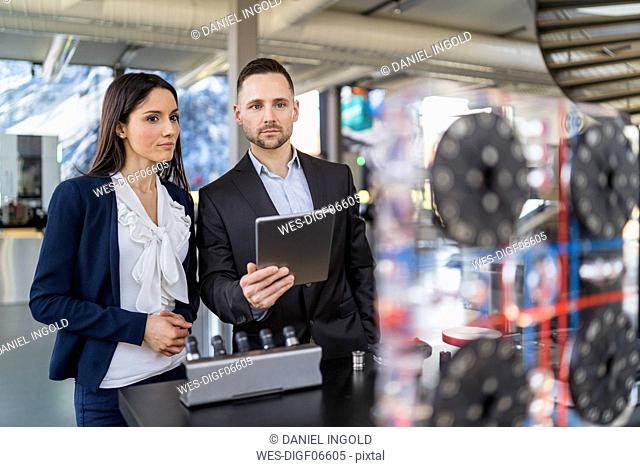 Businessman and businesswoman with tablet looking at a machine in modern factory