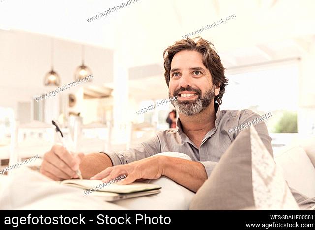 Smiling bearded man sitting on couch taking notes