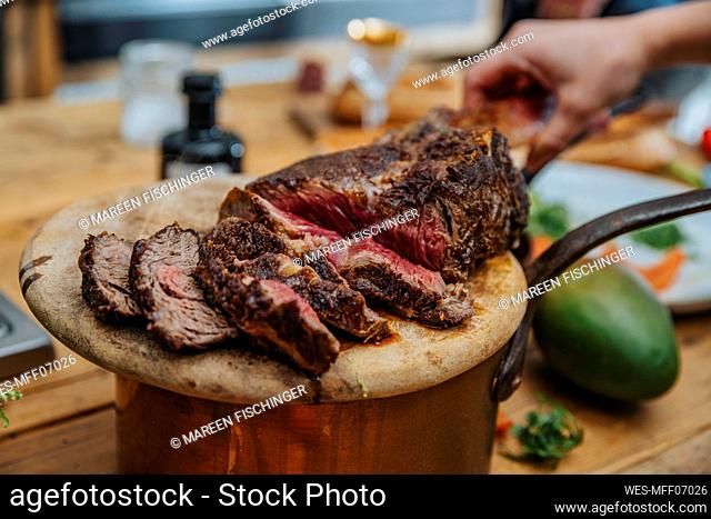 Chef arranging slice of cooked tomahawk steak in wooden plate at kitchen