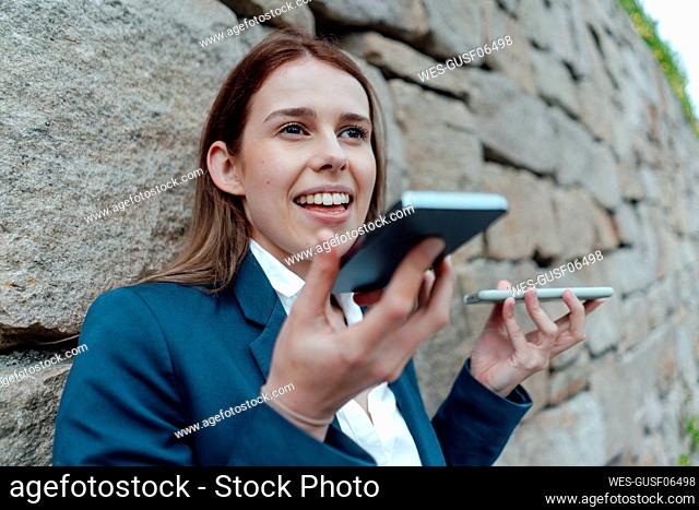 Female freelancer talking on smart phones while leaning on wall