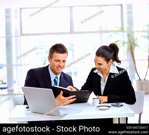 Businessman and businesswoman having a meeting in office lobby, drinking coffee