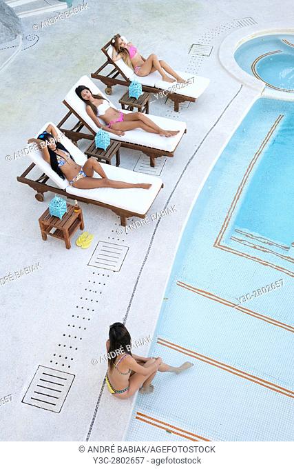 Four young women tanning and enjoying day at swimming pool