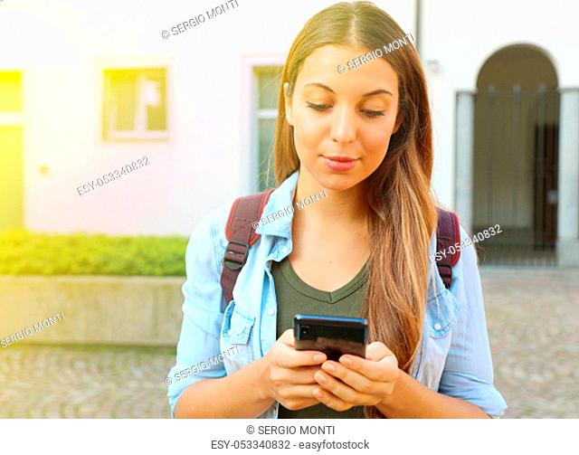 Beautiful young student girl typing on smart phone outdoors. Copy space