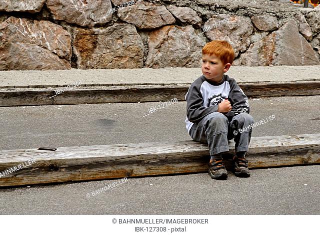 Little boy sits sad and lonesome at the street and is pouting