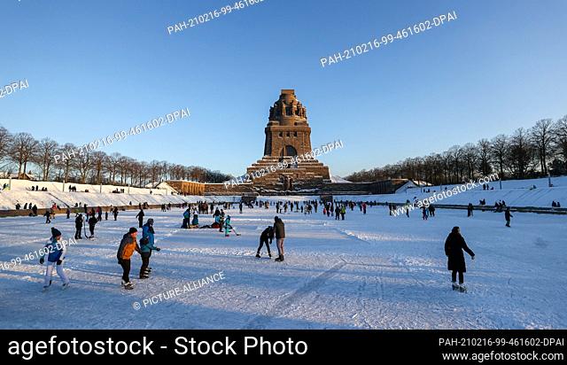 13 February 2021, Saxony, Leipzig: Leipzigers skate across the ice on the Lake of a Thousand Tears in front of the Monument to the Battle of the Nations