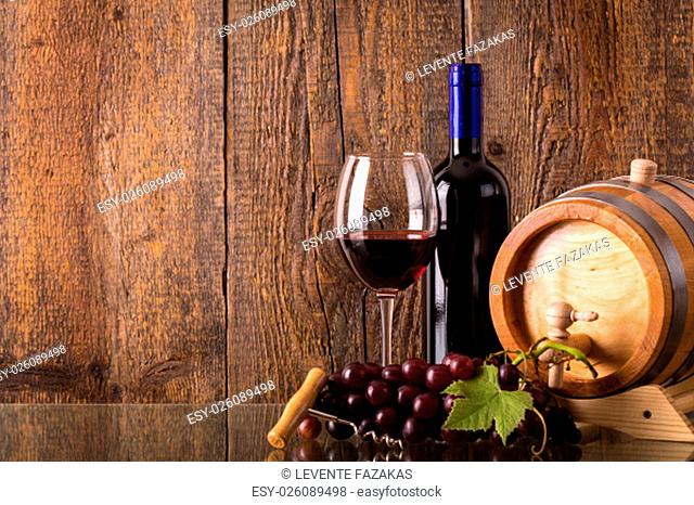 Glass of red wine with bottle barrel grapes and wooden background
