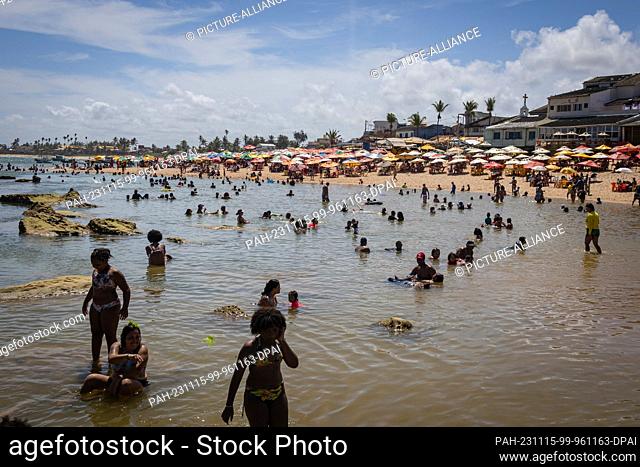 15 November 2023, Brazil, Salvador: Numerous people bathe in the sea and sit under parasols on Arembepe beach in the middle of the week