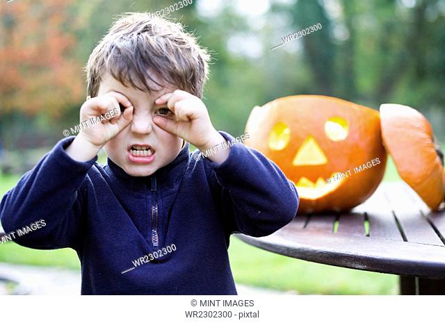 A boy looking through his curved fingers beside a carved pumpkin lantern
