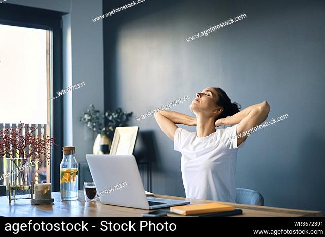Tired businesswoman with hands behind head sitting at desk in home office