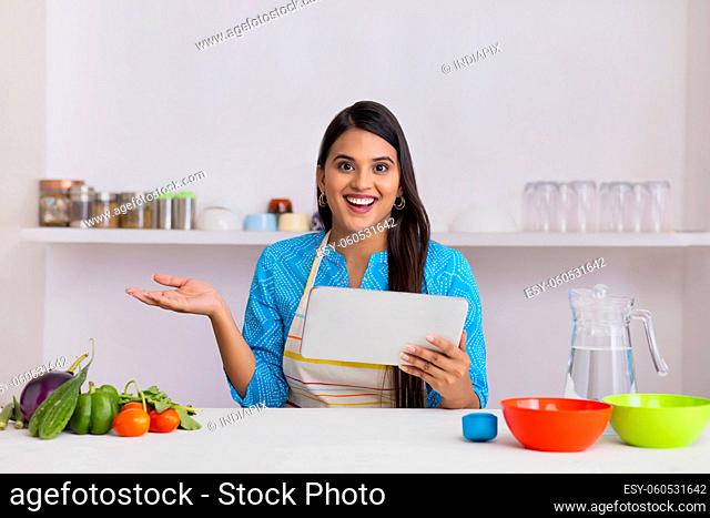 Indian woman posing while learning recipe through tablet in kitchen