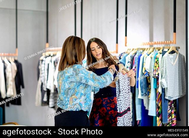 Female shopkeeper assisting woman while holding dress in boutique