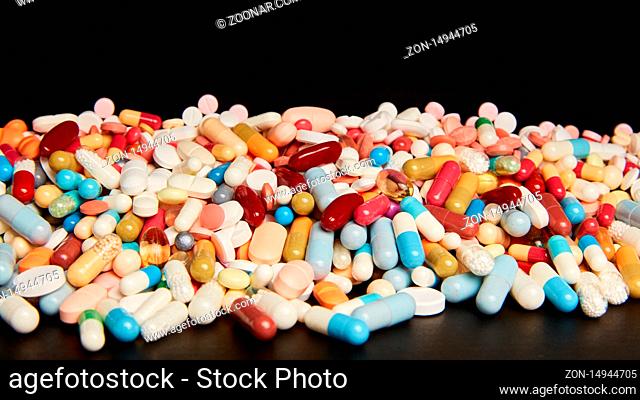 Tabletten und Pillen als bunte Medikamente vor einem dunklen Header Hintergrund