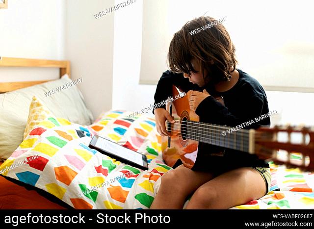Boy sitting on bed using digital tablet for playing song on guitar