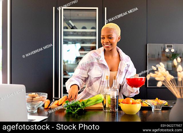 Happy african american woman cooking in kitchen, using laptop
