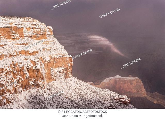 Grand Canyon National Park, AZ - Sunlight breaks through the clouds as snow falls in the Grand Canyon