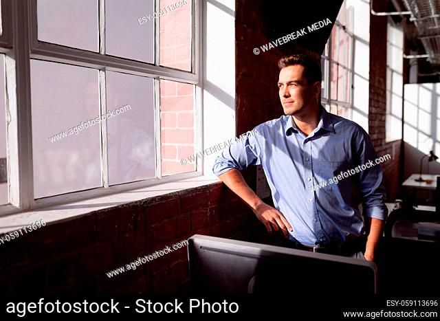 Thoughtful caucasian businessman standing in sunny office looking out of window