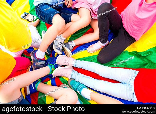Close view of children's legs laying in a circle on a rainbow parachute. After school outdoor activities