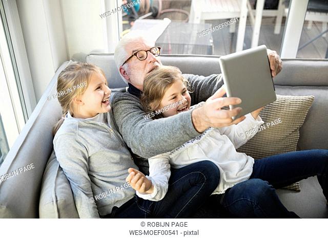 Two happy girls and grandfather on sofa taking a selfie with tablet