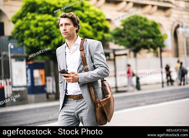 Man with bag using mobile phone while walking in city