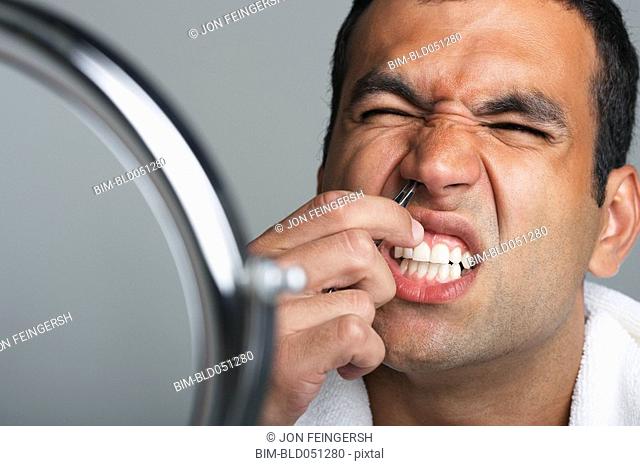 Hispanic man tweezing nose hairs
