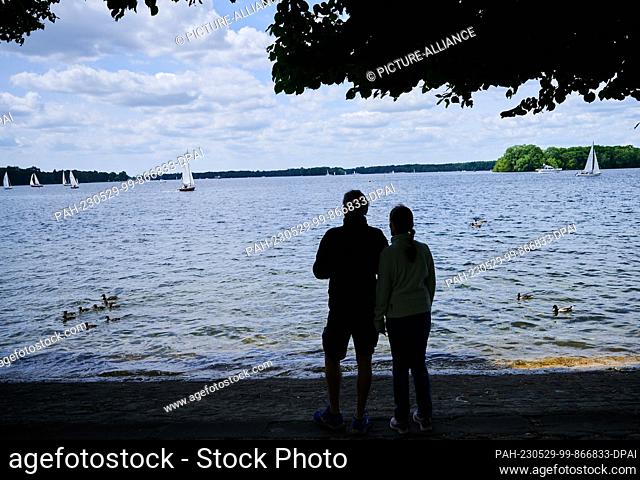 29 May 2023, Berlin: A couple stands on the shore of Lake Tegel, on which a family of ducks and sailboats are swimming. The beautiful weather on Whit Monday...