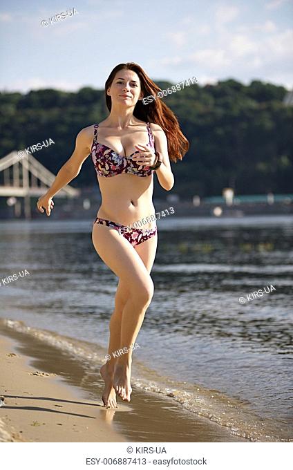 Woman running by the river beach at sunset