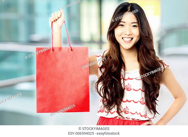Young trendy girl holding up red shopping bag