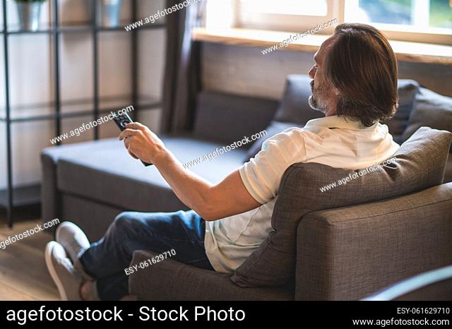 Watching tv. Man spending time at home and swithcing on tv with a tv remote