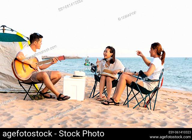 Happy friend have fun playing guitar and clap in camp they smiling together in holiday on sand beach near camping tent vacation time at sunset