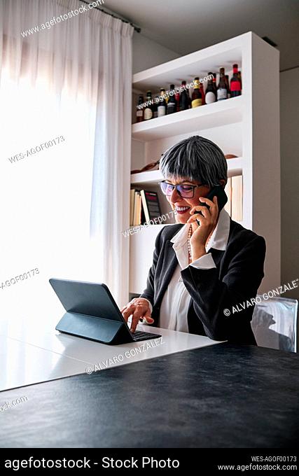 Businesswoman using digital tablet talking on smart phone at home