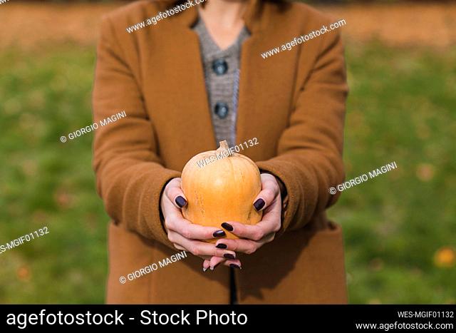 Young woman holding pumpkin in public park