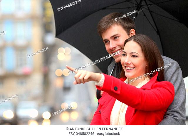Happy couple pointing away under the rain in winter