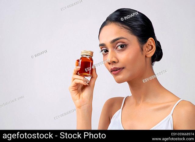 A young woman with clear, spotless skin holding a bottle of honey