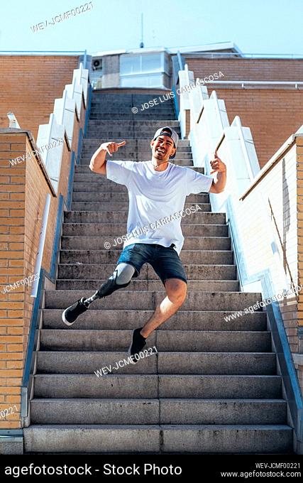 Happy young man with leg prosthesis jumping on stairs inb the city