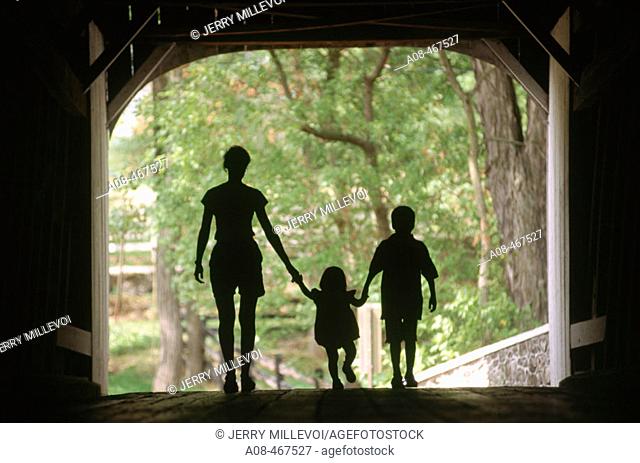 Silhouette of mom with two children in covered bridge. Pennsylvania, USA