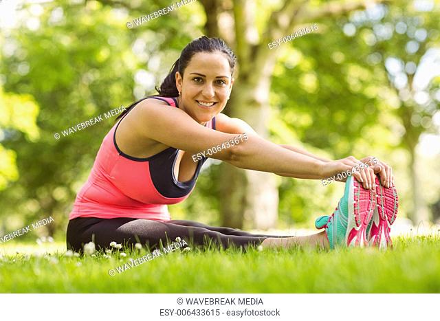Happy brunette in sportswear stretching on the grass