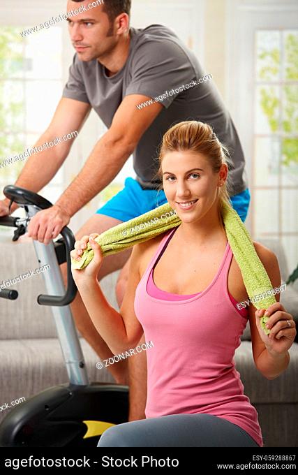 Man training on exercise bike, woman doing streching exercise on fitness mat at home