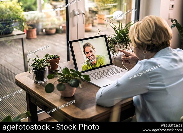 Grandmother gesturing while talking to grandson on video call through laptop on table at home