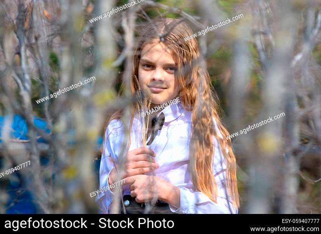 A girl stands with dried wildflowers, in the foreground blurred branches of bushes