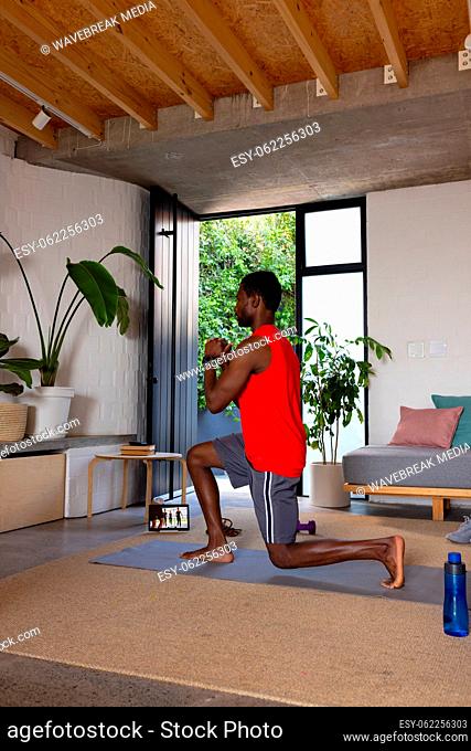 African american man exercising in living room, using tablet